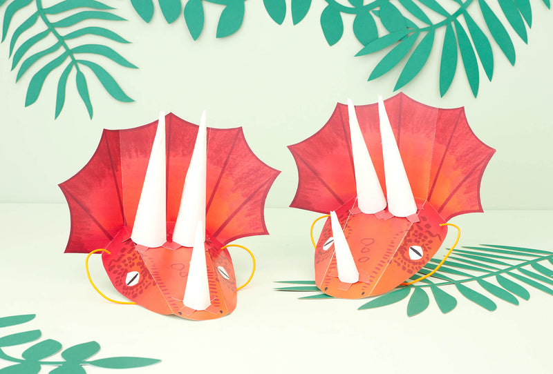 A light green backdrop with dark green leaves and two triceratops headpieces made of red card and white card tusks.