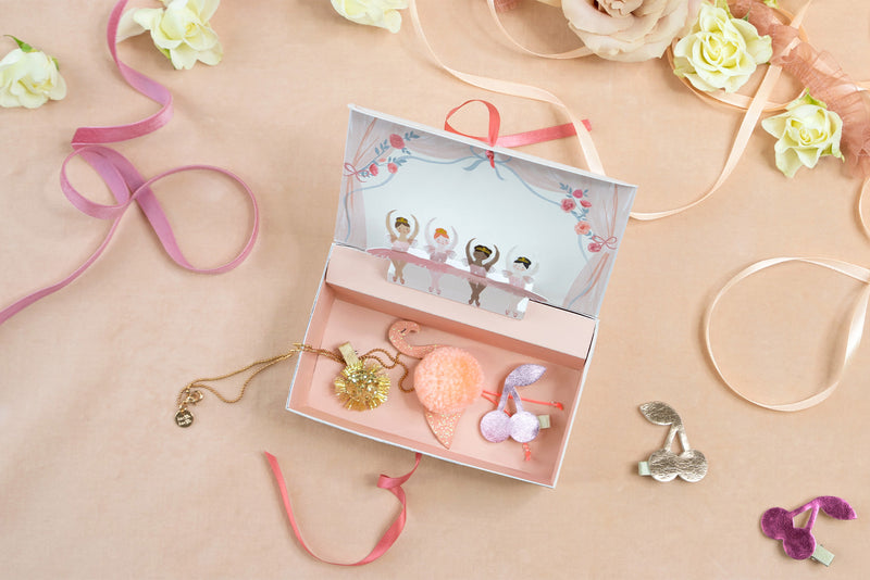 A dusty pink jewellery box with a line of ballerina characters along the top filled with accessories against a backdrop of light pink and ribbons.