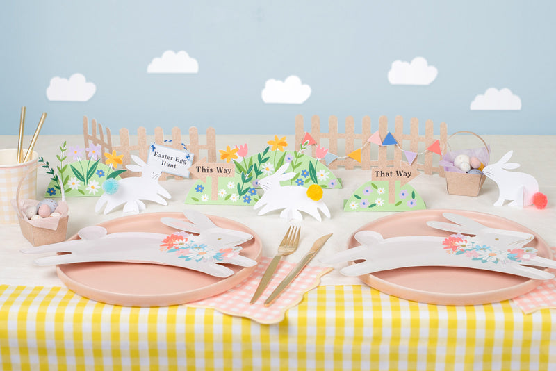 A yellow and white striped table is decorated with pink and leaping bunny plates. Cardboard floral and bunny decorations are placed in the centre.