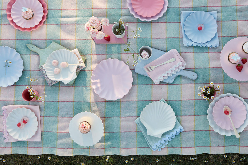 A checker cloth is decorated with pastel pink and blue seashell and scallop-edged reusable plates and linen napkins.