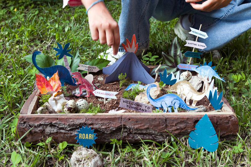 A small container filled with cardboard dinosaurs and prehistoric-inspired accessories.