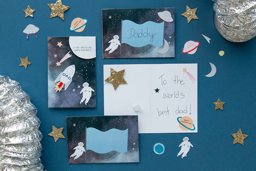 A navy background is covered by gold stars and father's day cards which feature space designs such as rocket ships and spacemen.