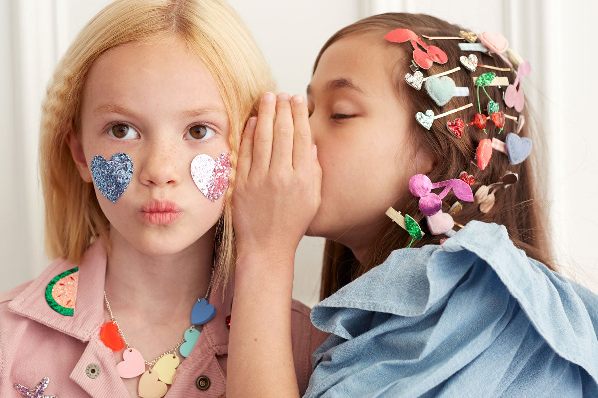 Two girls wear accessories, including felt hair slides and heart hair grips, and a heart necklace.
