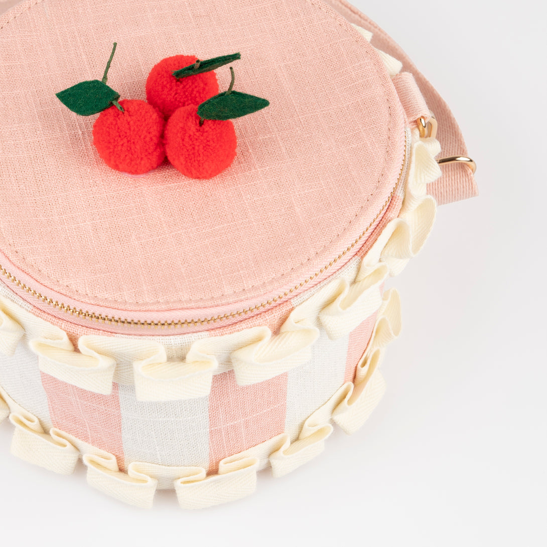 Our pink fabric bag, crafted to look like a cake, features fun pompom cherries, felt leaves, a ruffled ribbon and a long webbing handle.