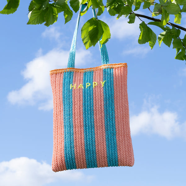 Our raffia bag, made from paper based raffia with pink and blue stripes, and an orange border, has the word Happy embroidered on the front. Image1