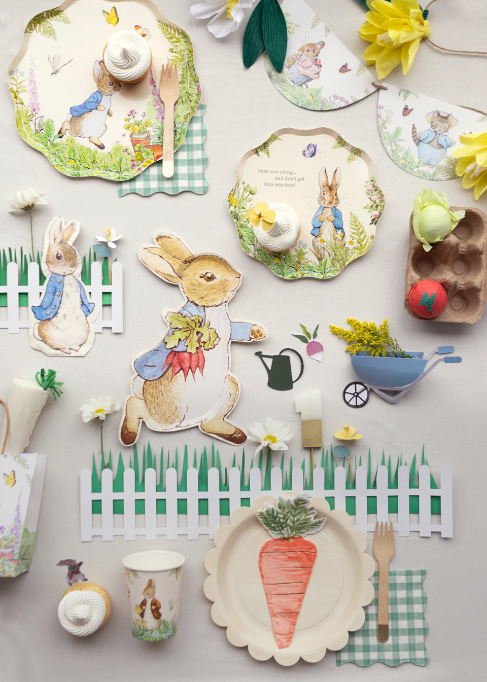 Peter Rabbit decorations are placed across a table, including Peter Rabbit plates, garlands, cups, party bags, and napkins.